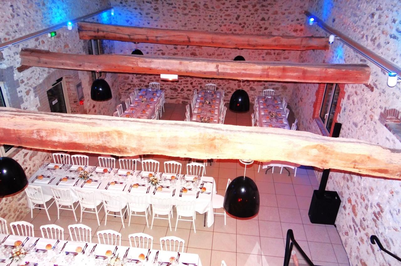 Location salle La Villeneuve-en-Chevrie (Yvelines) - La Grange des Mollières #36 Salle de réception en pierre avec poutres apparentes, tables dressées et chaises blanches alignées pour un événement.