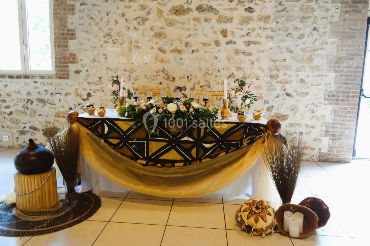 Location salle La Villeneuve-en-Chevrie (Yvelines) - La Grange des Mollières #39 Table décorée avec des fleurs, bougies et tissus dorés, dans une salle en pierre avec lumière naturelle.