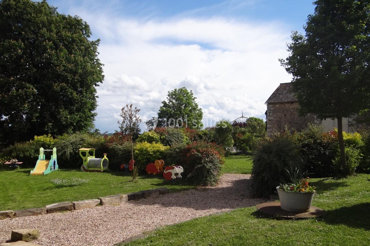 Location salle La Villeneuve-en-Chevrie (Yvelines) - La Grange des Mollières #41 Jardin avec pelouse, jeux pour enfants, arbres et arbustes, sous un ciel bleu partiellement nuageux.
