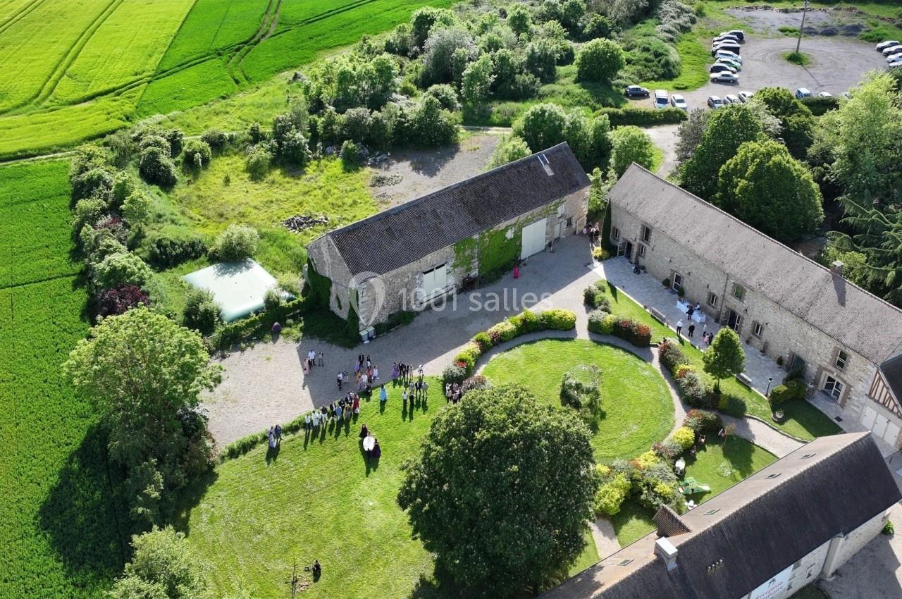 Location salle La Villeneuve-en-Chevrie (Yvelines) - La Grange des Mollières #42 Vue aérienne d'une ferme avec bâtiments en pierre, cour centrale, pelouse, jardins et champs environnants.