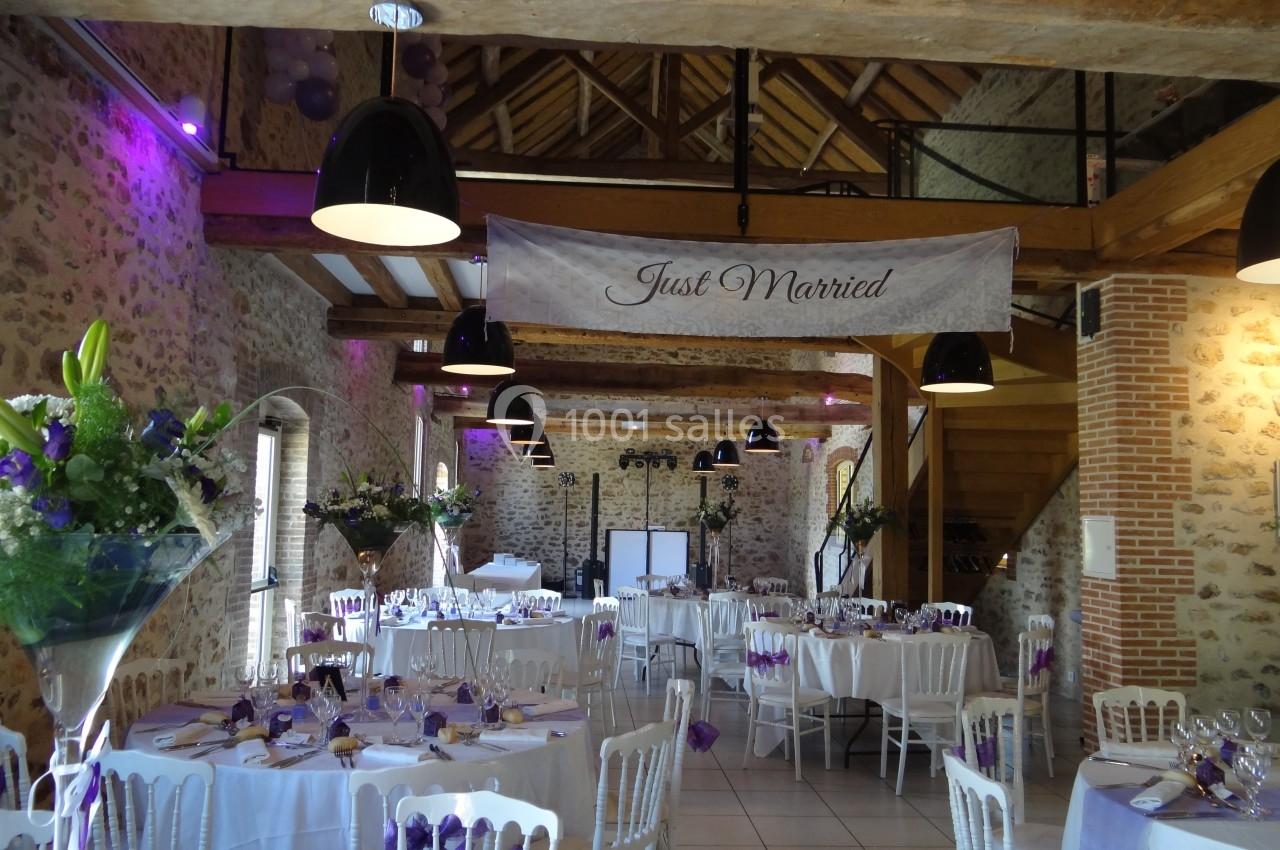Location salle La Villeneuve-en-Chevrie (Yvelines) - La Grange des Mollières #43 Salle de réception décorée pour un mariage, avec tables dressées, fleurs violettes et une bannière ’Just Married’.