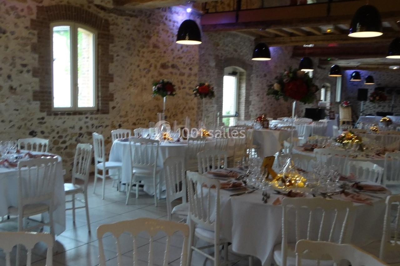 Location salle La Villeneuve-en-Chevrie (Yvelines) - La Grange des Mollières #44 Salle de réception en pierre avec tables rondes dressées, décorations florales et éclairage suspendu.