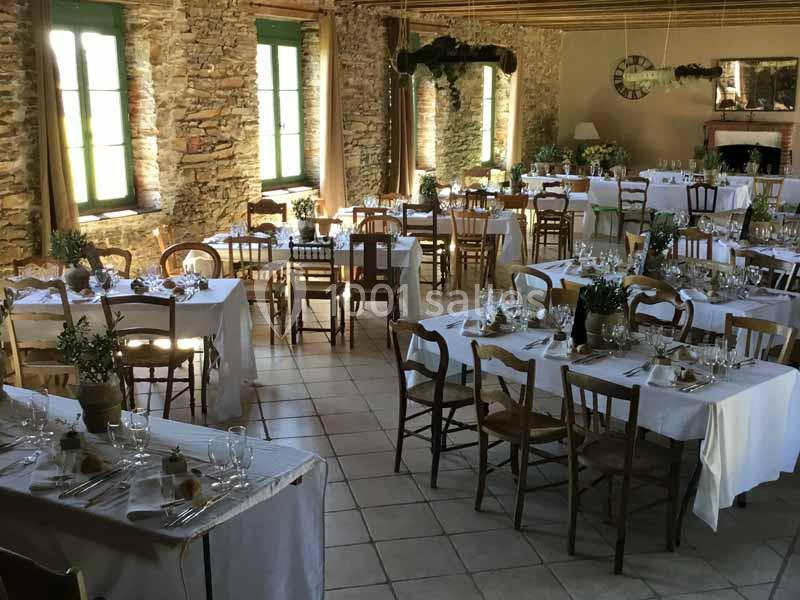 Location salle Haute-Goulaine (Loire-Atlantique) - La Cour des Montys #13 Salle de réception rustique avec tables dressées, nappes blanches, chaises en bois et murs en pierre apparente.