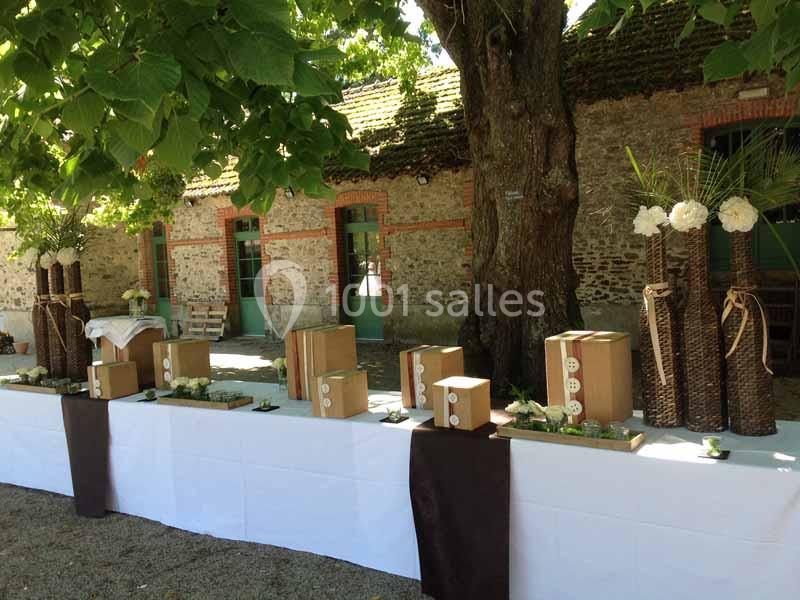 Location salle Haute-Goulaine (Loire-Atlantique) - La Cour des Montys #18 Table décorée en extérieur avec des boîtes en bois, des vases en osier et des fleurs blanches sous un grand arbre.