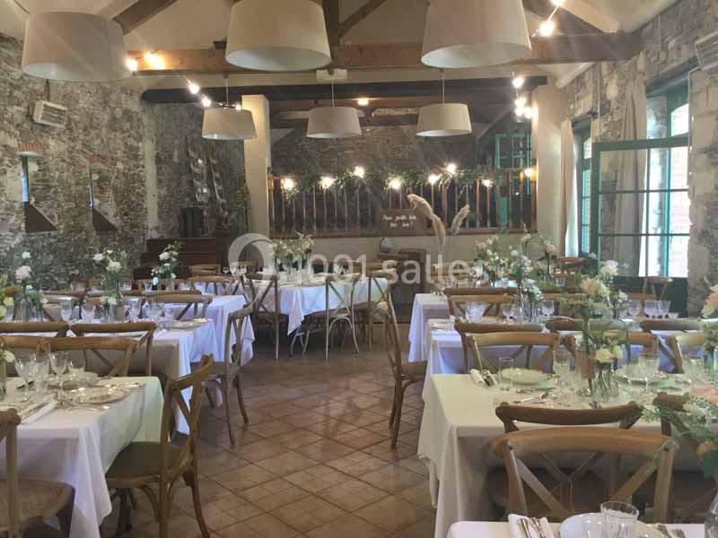 Location salle Haute-Goulaine (Loire-Atlantique) - La Cour des Montys #4 Salle de réception décorée pour un événement, avec tables dressées, chaises en bois et murs en pierre apparente.