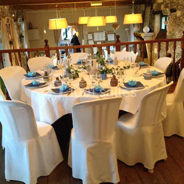 Location salle Haute-Goulaine (Loire-Atlantique) - La Cour des Montys #10 Table ronde élégamment dressée avec nappes blanches, serviettes bleues et décorations, dans une salle lumineuse en bois.