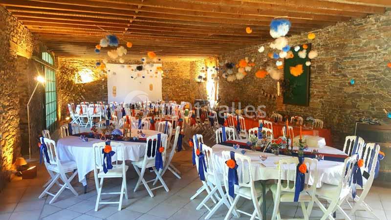 Location salle Haute-Goulaine (Loire-Atlantique) - La Cour des Montys #12 Salle en pierre décorée pour un événement, avec tables rondes dressées, chaises blanches et suspensions colorées.