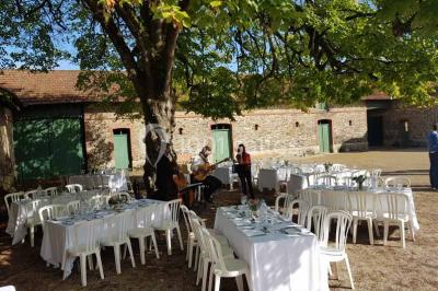Miniature Location salle Haute-Goulaine (Loire-Atlantique) - La Cour des Montys #17 Cour extérieure éclairée en soirée, avec un grand arbre central, des tables, des palettes en bois et des invités debout.