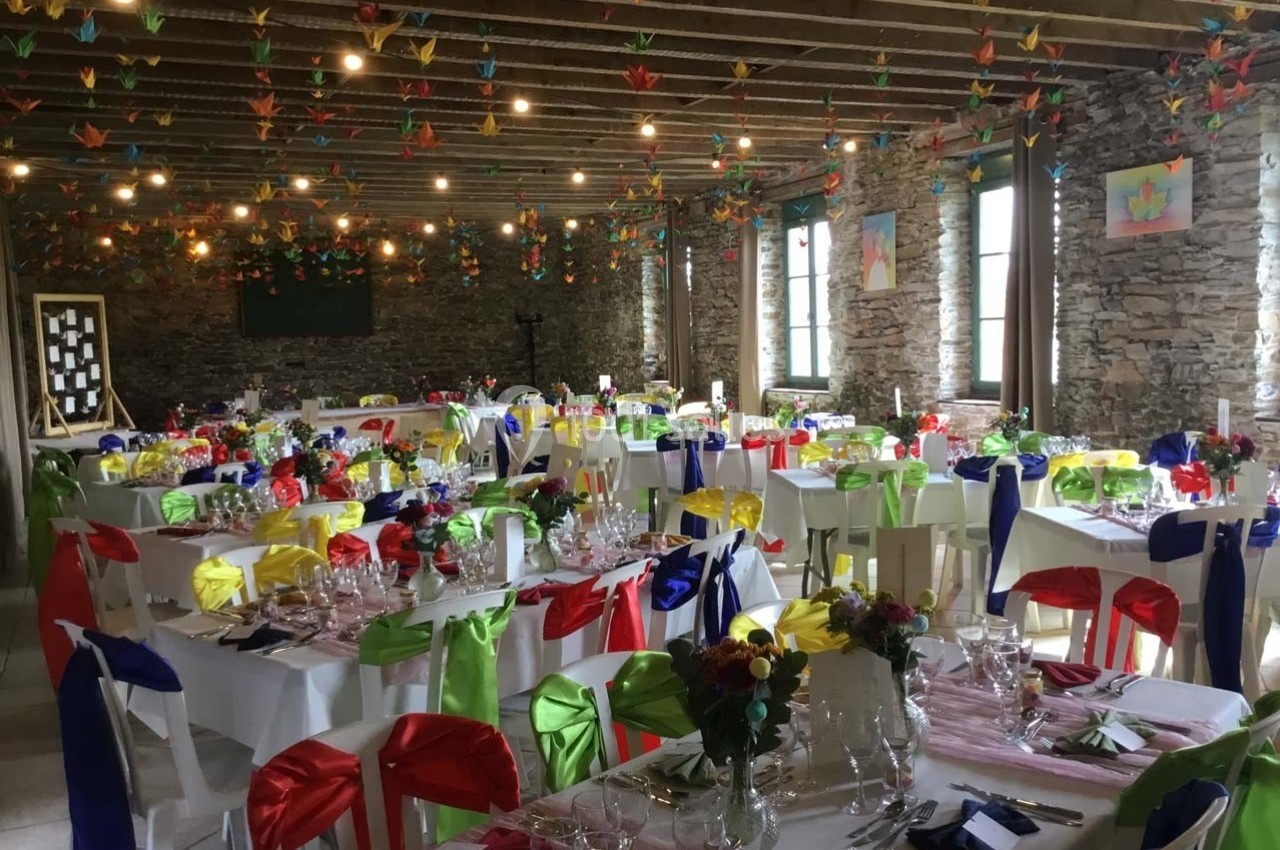 Salle de réception décorée avec des tables dressées, des nappes colorées et des guirlandes de grues en papier suspendues.