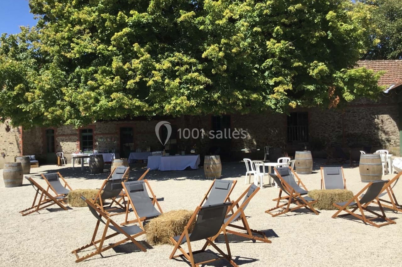 Chaises longues disposées en cercle sur un sol gravillonné, sous de grands arbres devant un bâtiment en pierre.