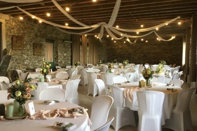 Un groupe de personnes rassemblées sous de grands arbres devant des bâtiments en pierre par une journée ensoleillée.