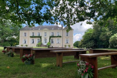 Un groupe de personnes rassemblées sous de grands arbres devant des bâtiments en pierre par une journée ensoleillée.