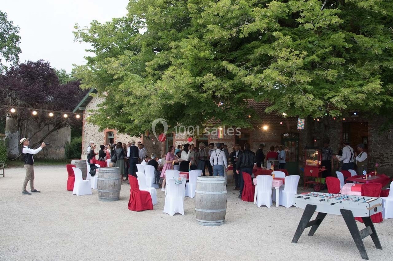 Groupe de personnes rassemblées dans une cour extérieure décorée, avec tables, chaises et guirlandes lumineuses.