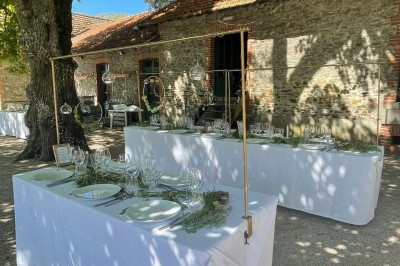 Un groupe de personnes rassemblées sous de grands arbres devant des bâtiments en pierre par une journée ensoleillée.