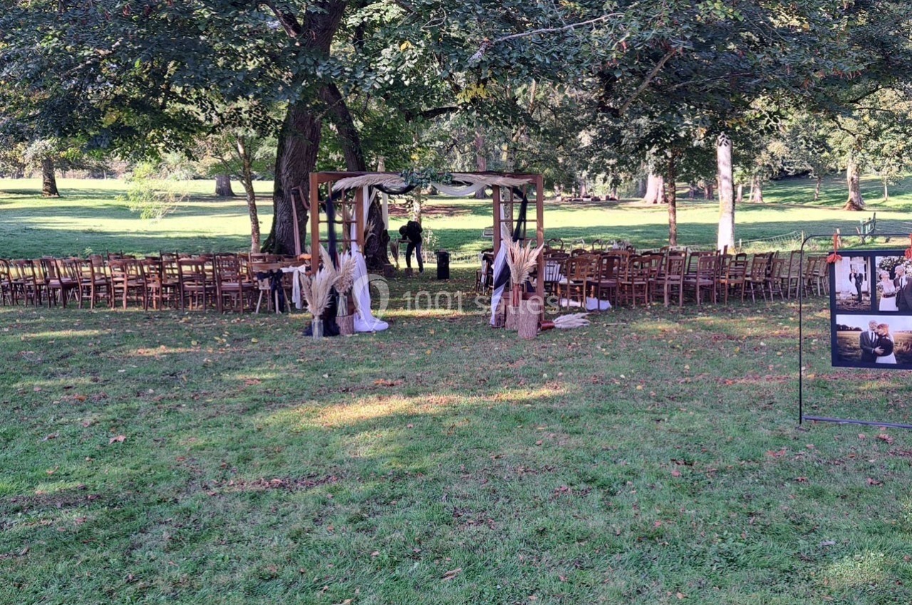 Chaises disposées en extérieur sous des arbres autour d'une arche décorée pour une cérémonie en plein air.