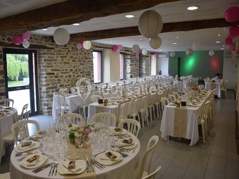 Salle de réception décorée avec des tables dressées, des chaises blanches et des lanternes suspendues.