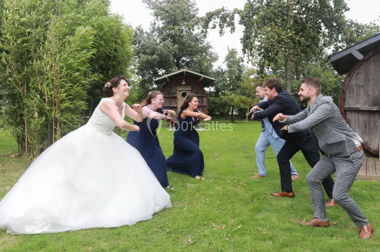 Des personnes en tenue de mariage s'amusent en imitant une danse ou un jeu dans un jardin verdoyant.