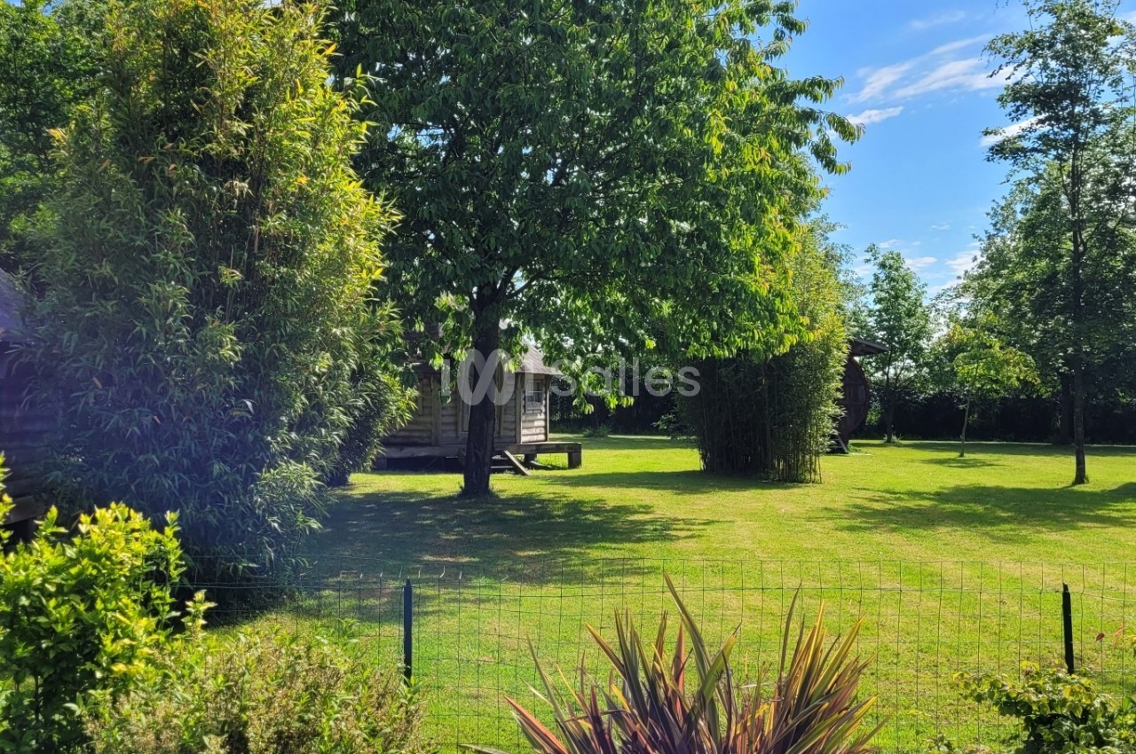 Espace vert avec cabanes en bois, arbres et arbustes sous un ciel ensoleillé.