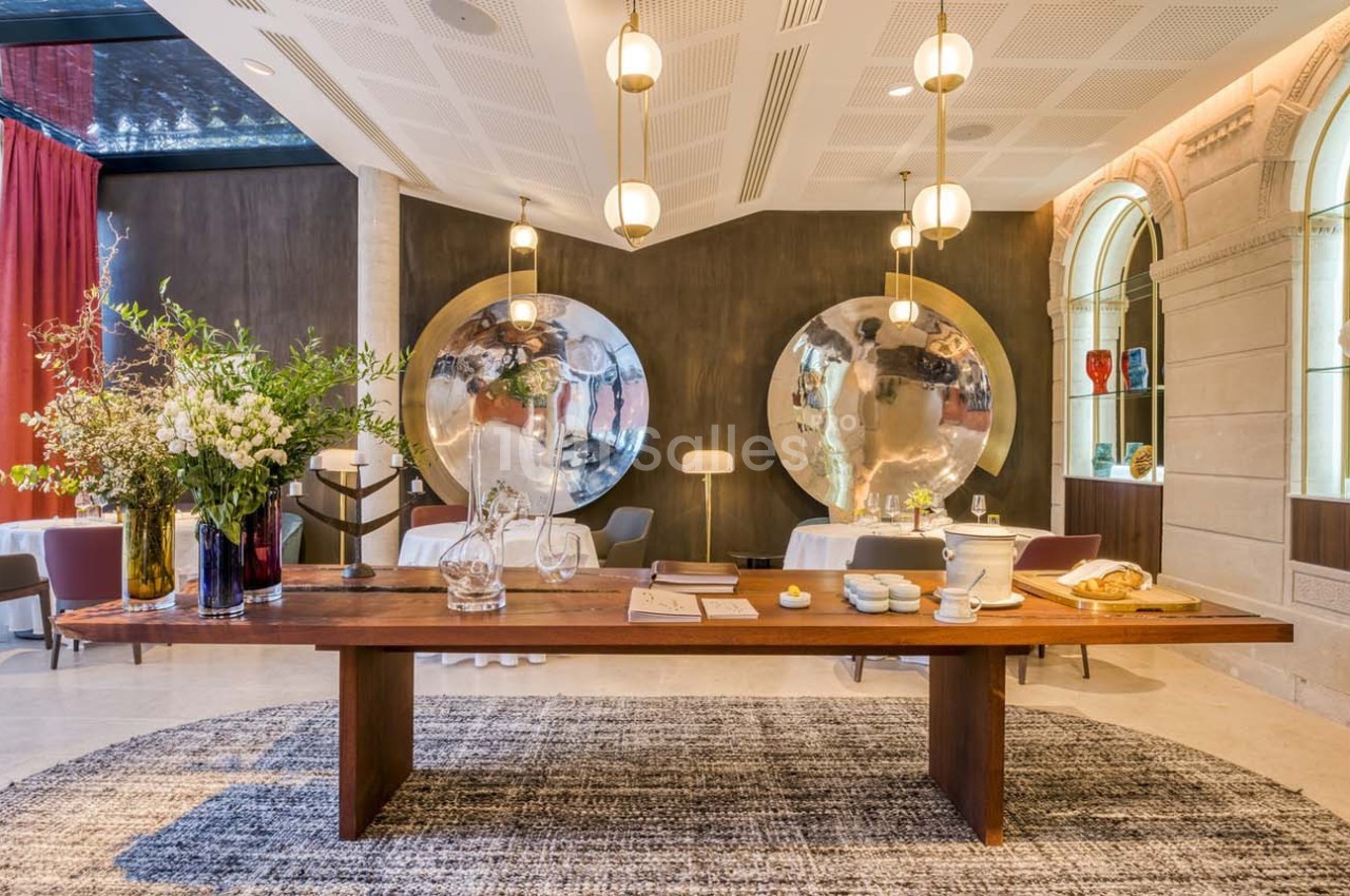Table en bois avec objets décoratifs, entourée de luminaires suspendus et de miroirs ronds dans une salle élégante.