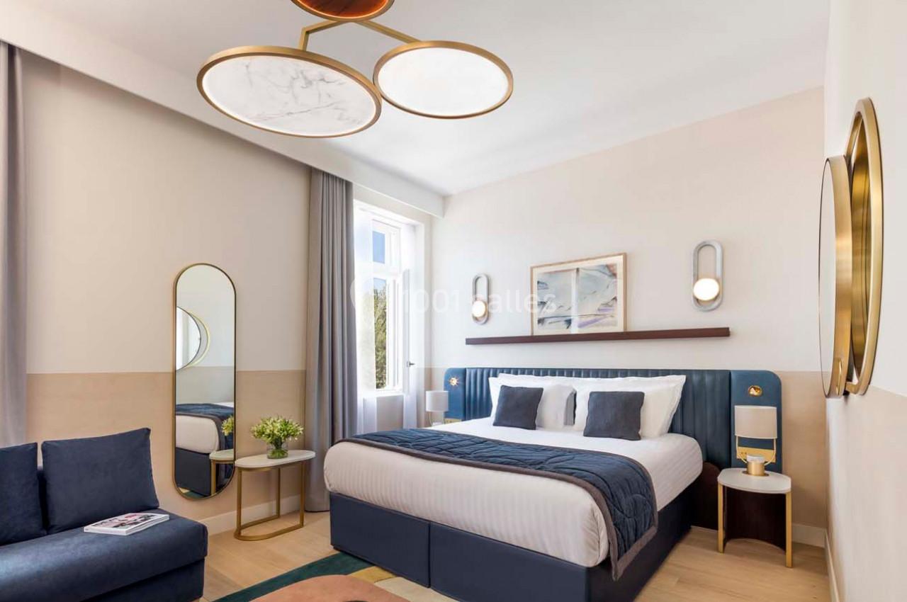 Chambre lumineuse avec lit double, canapé, table basse, miroir, et décoration moderne dans des tons neutres et bleus.