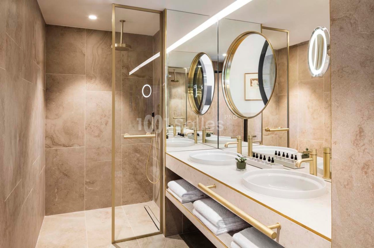 Salle de bain moderne avec double vasque, miroirs ronds, douche à paroi vitrée et finitions dorées.