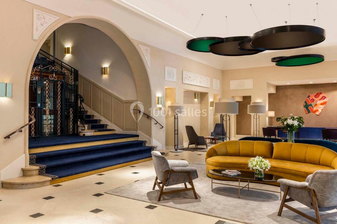 Hall d'entrée élégant avec escalier, canapé jaune, fauteuils et luminaires modernes dans un décor lumineux.