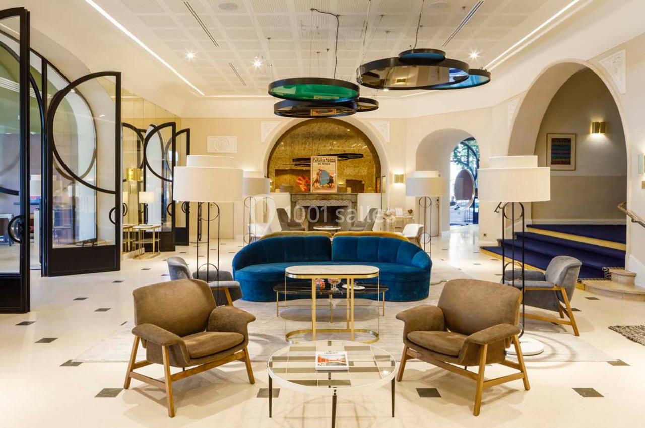 Salon élégant avec fauteuils, canapé bleu, tables basses, éclairage design et décorations modernes dans un espace lumineux.