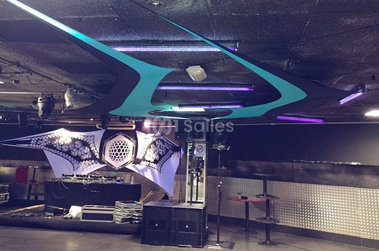 Salle de concert avec scène équipée de matériel audio, décorations lumineuses et plafond aux motifs futuristes.
