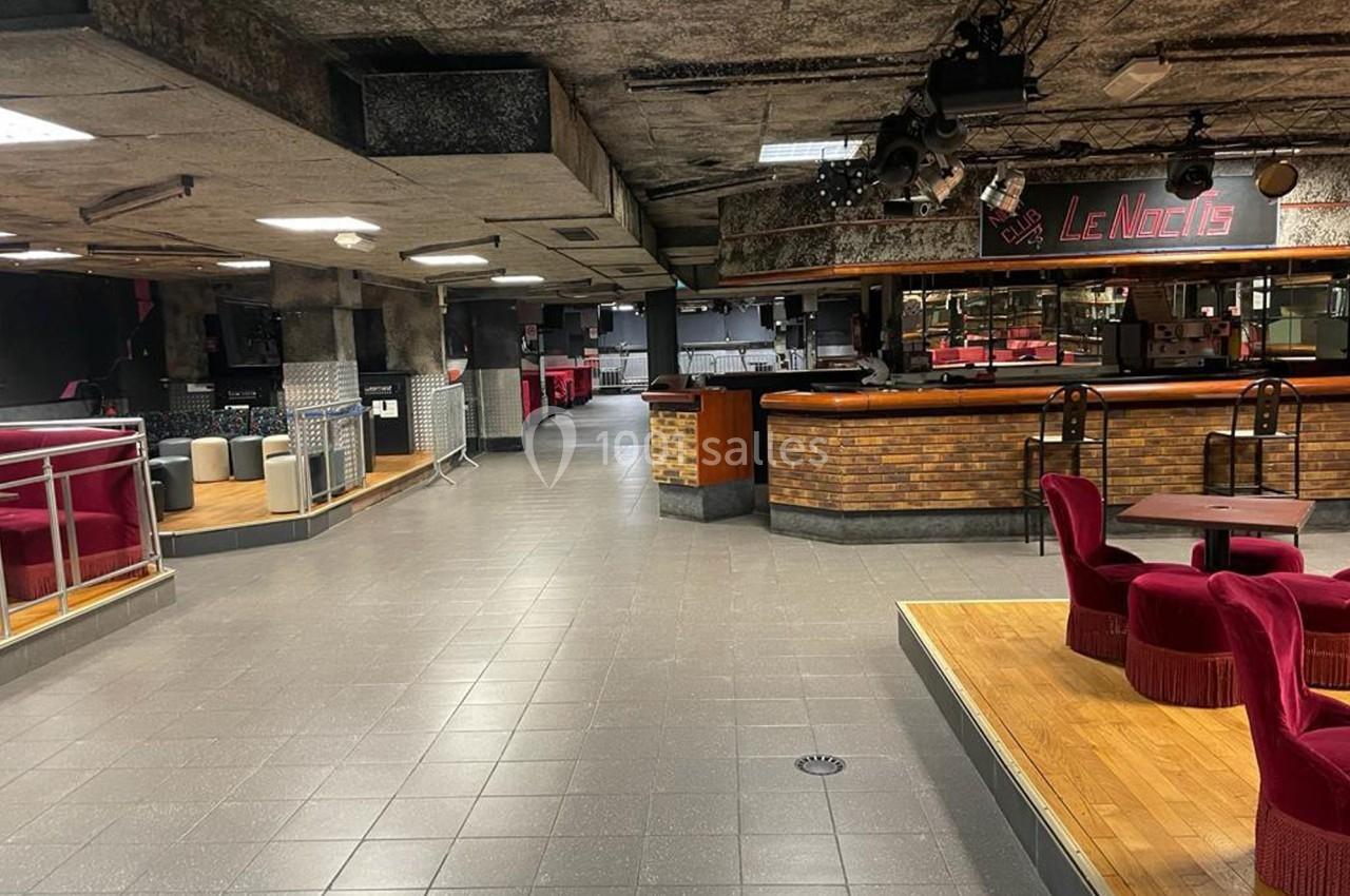 Intérieur d'une discothèque vide avec bar en briques, tables, chaises rouges et éclairage tamisé.