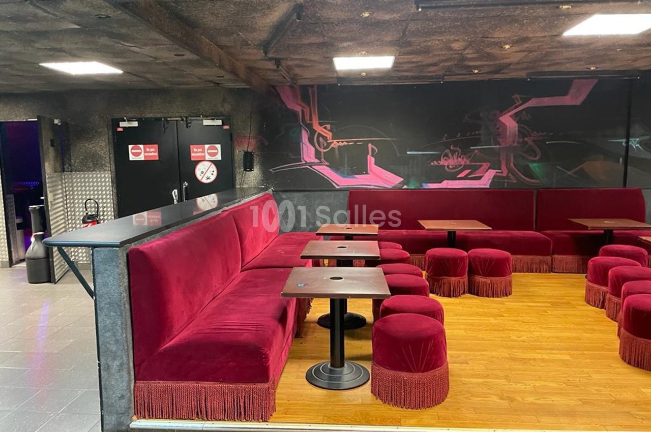 Banquettes rouges avec franges, tables en bois et tabourets assortis dans un espace intérieur à la décoration sombre.
