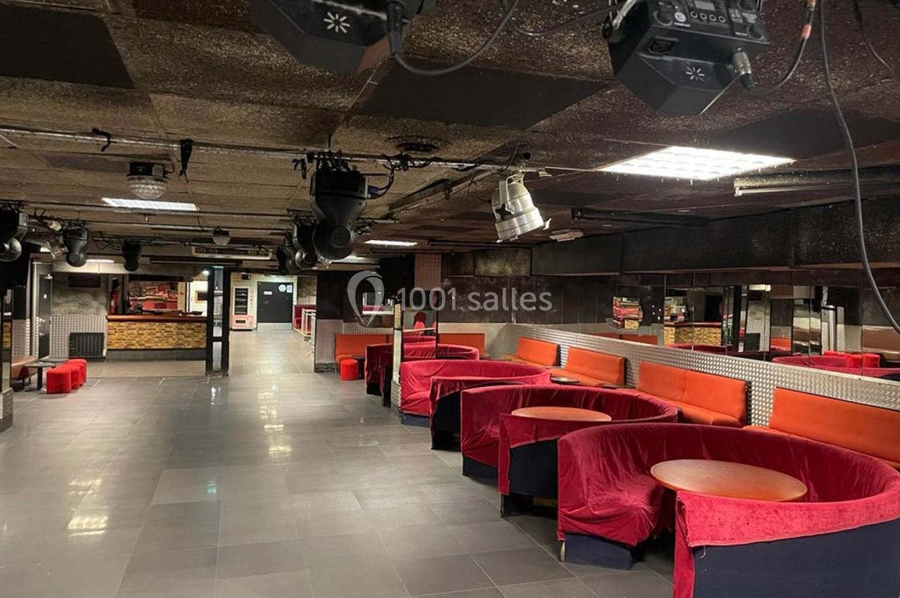 Salle de discothèque vide avec banquettes rouges, tables rondes et éclairages suspendus au plafond.