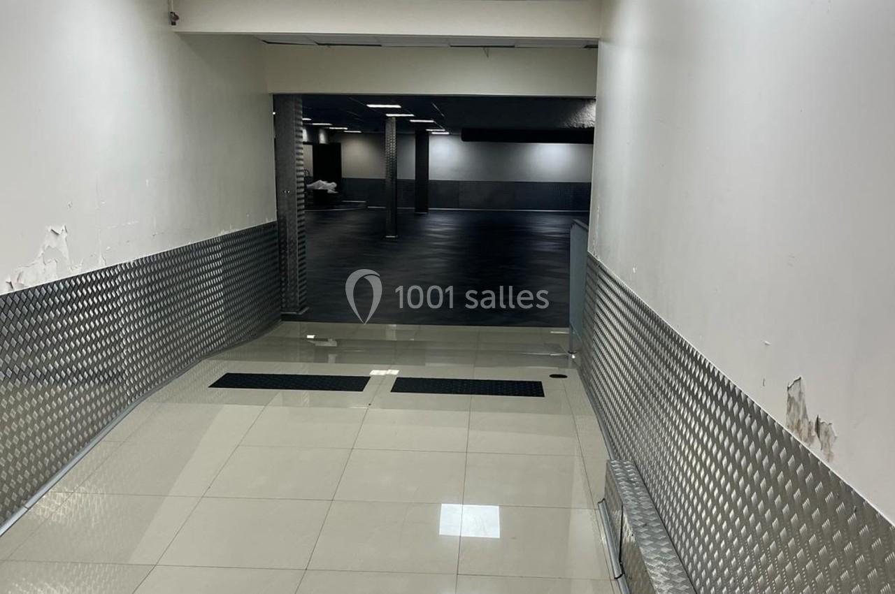 Rampe inclinée avec revêtement métallique menant à un espace intérieur sombre au sol noir et murs clairs.