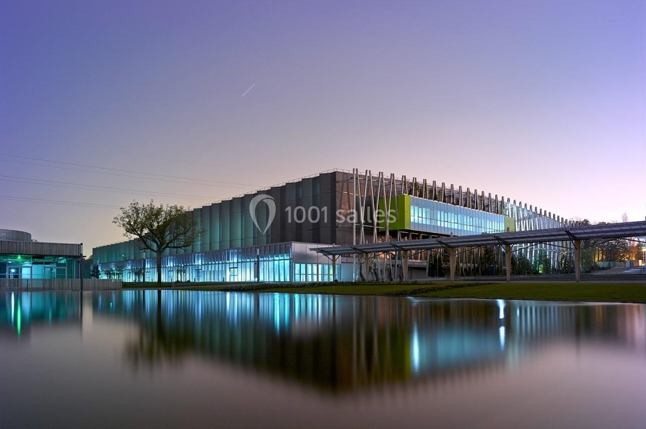 Location salle Nantes (Loire-Atlantique) - Exponantes Le Parc #20 Bâtiment moderne avec façade vitrée, éclairé au crépuscule, reflété dans un plan d'eau calme.