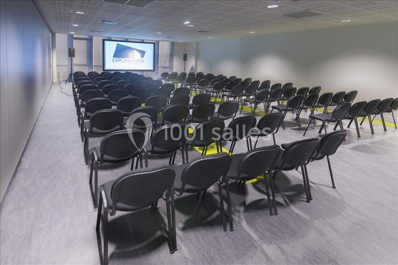 Location salle Nantes (Loire-Atlantique) - Exponantes Le Parc #9 Salle de conférence vide avec des rangées de chaises noires orientées vers un écran de projection allumé.