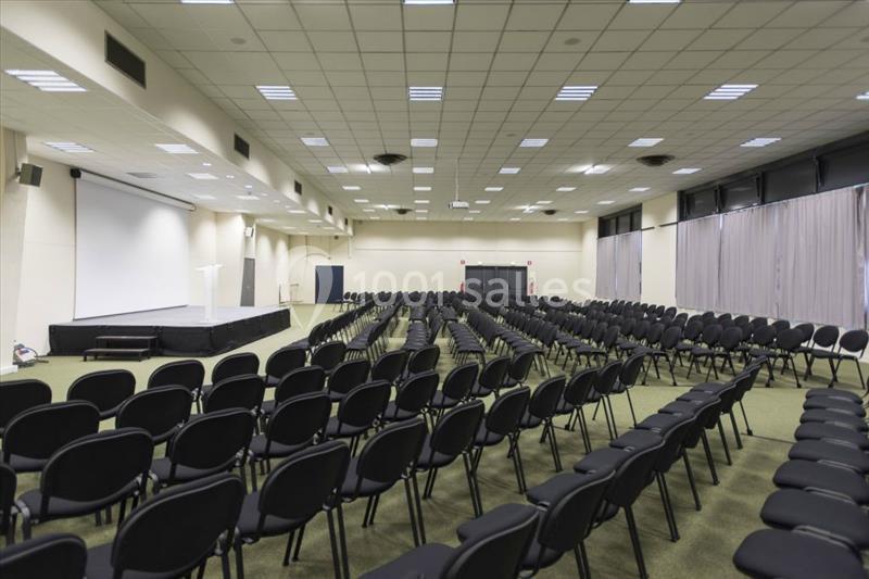 Location salle Nantes (Loire-Atlantique) - Exponantes Le Parc #13 Salle de conférence vide avec des rangées de chaises noires alignées et une estrade équipée d'un pupitre.