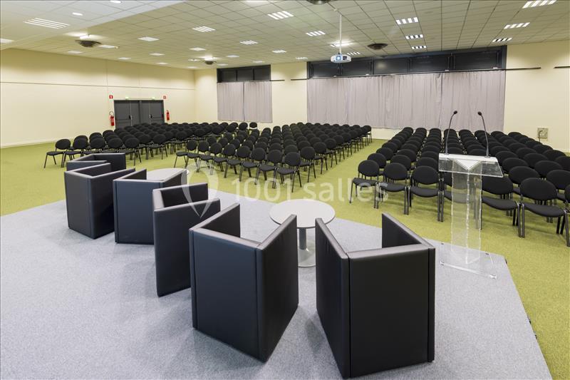Location salle Nantes (Loire-Atlantique) - Exponantes Le Parc #18 Salle de conférence avec chaises alignées, scène équipée de fauteuils, table basse et pupitre transparent.