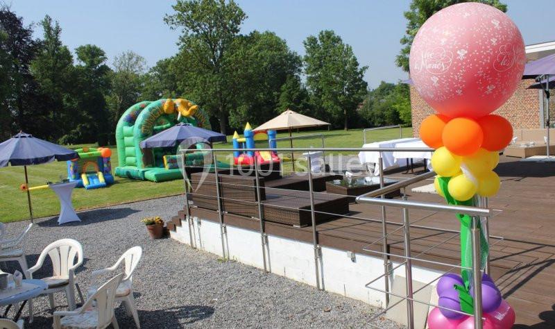 Location salle Donceel (Liège) - Château de Limont #20 Espace extérieur avec structures gonflables, terrasse en bois, tables et chaises sous parasols, décoré de ballons colorés.
