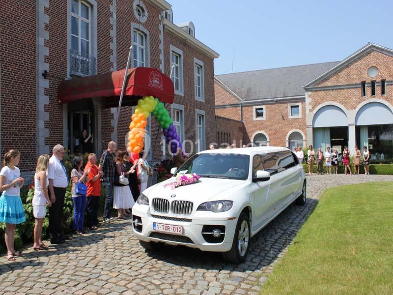 Location salle Donceel (Liège) - Château de Limont #9 Une limousine blanche décorée de fleurs arrive devant un bâtiment en briques, entourée de spectateurs.