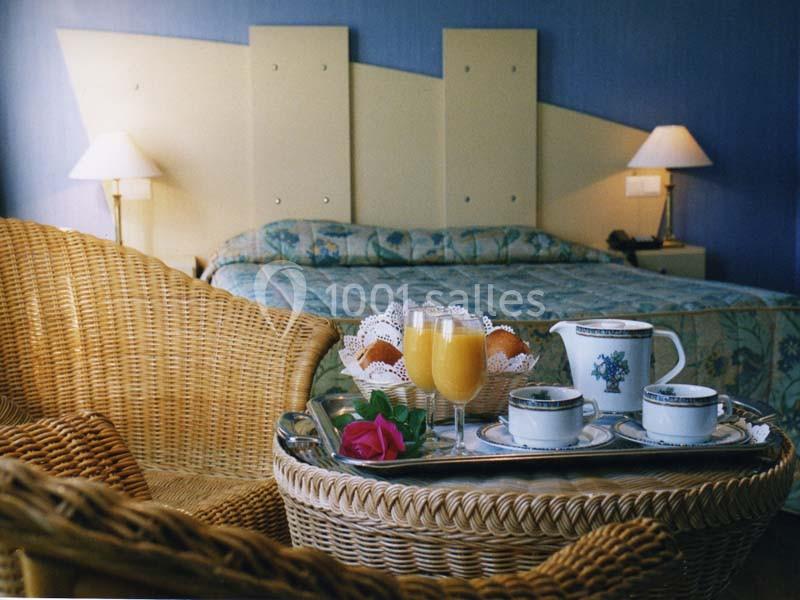 Location salle Donceel (Liège) - Château de Limont #10 Petit-déjeuner avec jus d'orange et café servi sur un plateau dans une chambre d'hôtel avec lit et fauteuils en osier.