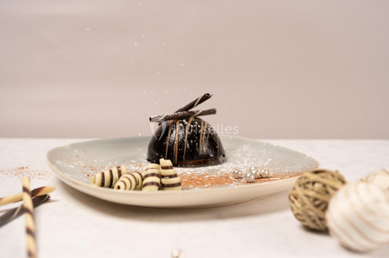 Location salle Donceel (Liège) - Château de Limont #18 Dessert au chocolat décoré de spirales en chocolat et saupoudré de sucre glace, présenté sur une assiette beige.