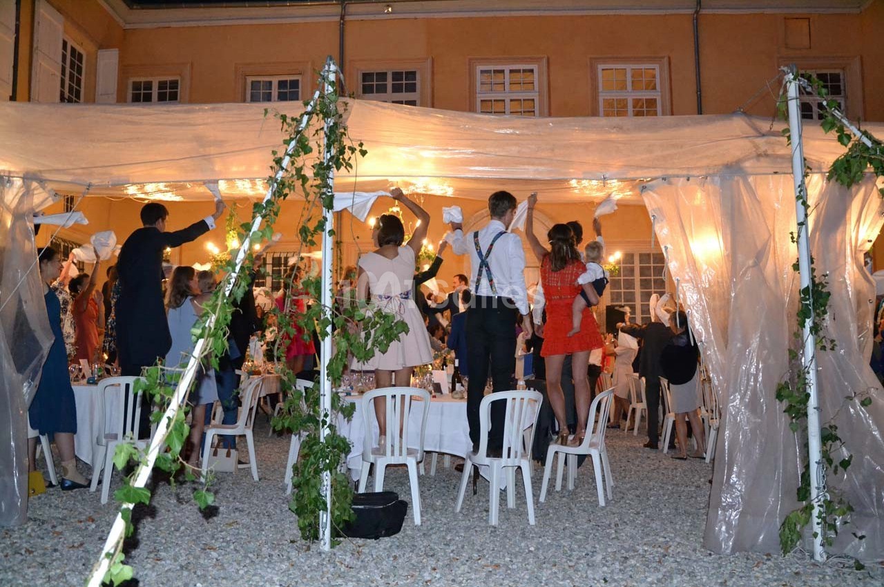 Des invités debout sous une tente éclairée, levant les bras lors d'une fête en soirée dans une cour pavée.