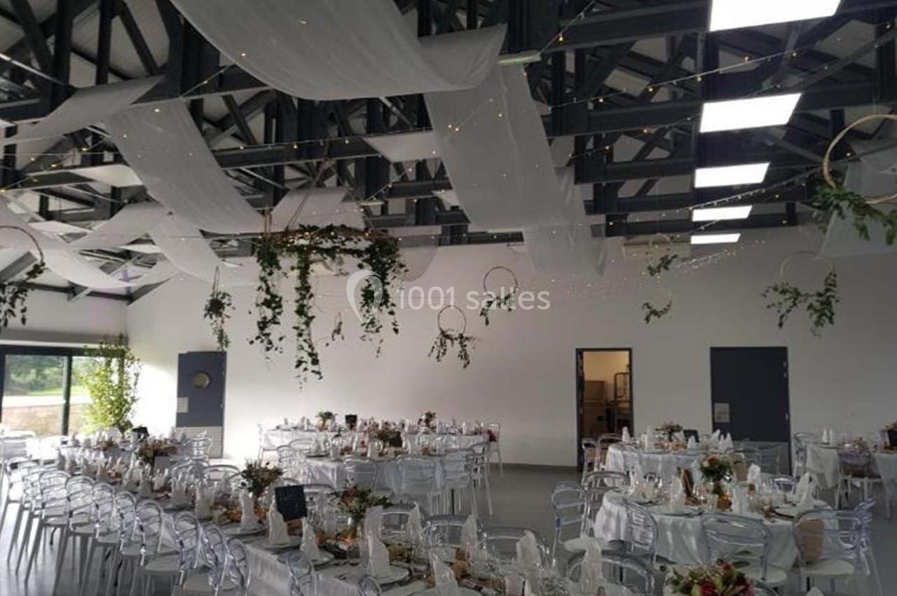 Salle de réception décorée avec des tables dressées, des voilages suspendus et des éléments végétaux.