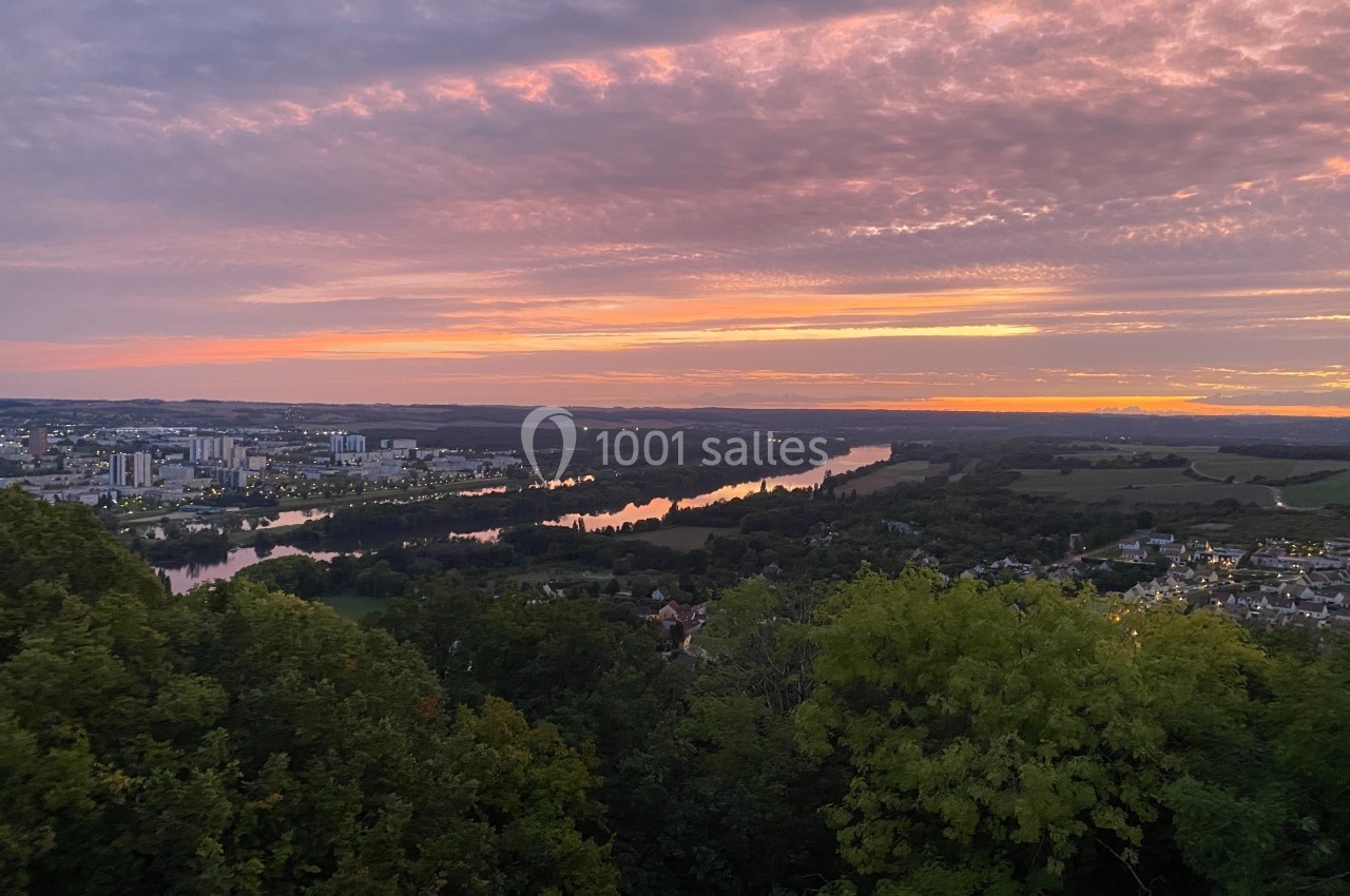Vue panoramique d'une rivière serpentant entre des villes et des champs sous un ciel coloré au coucher du soleil.