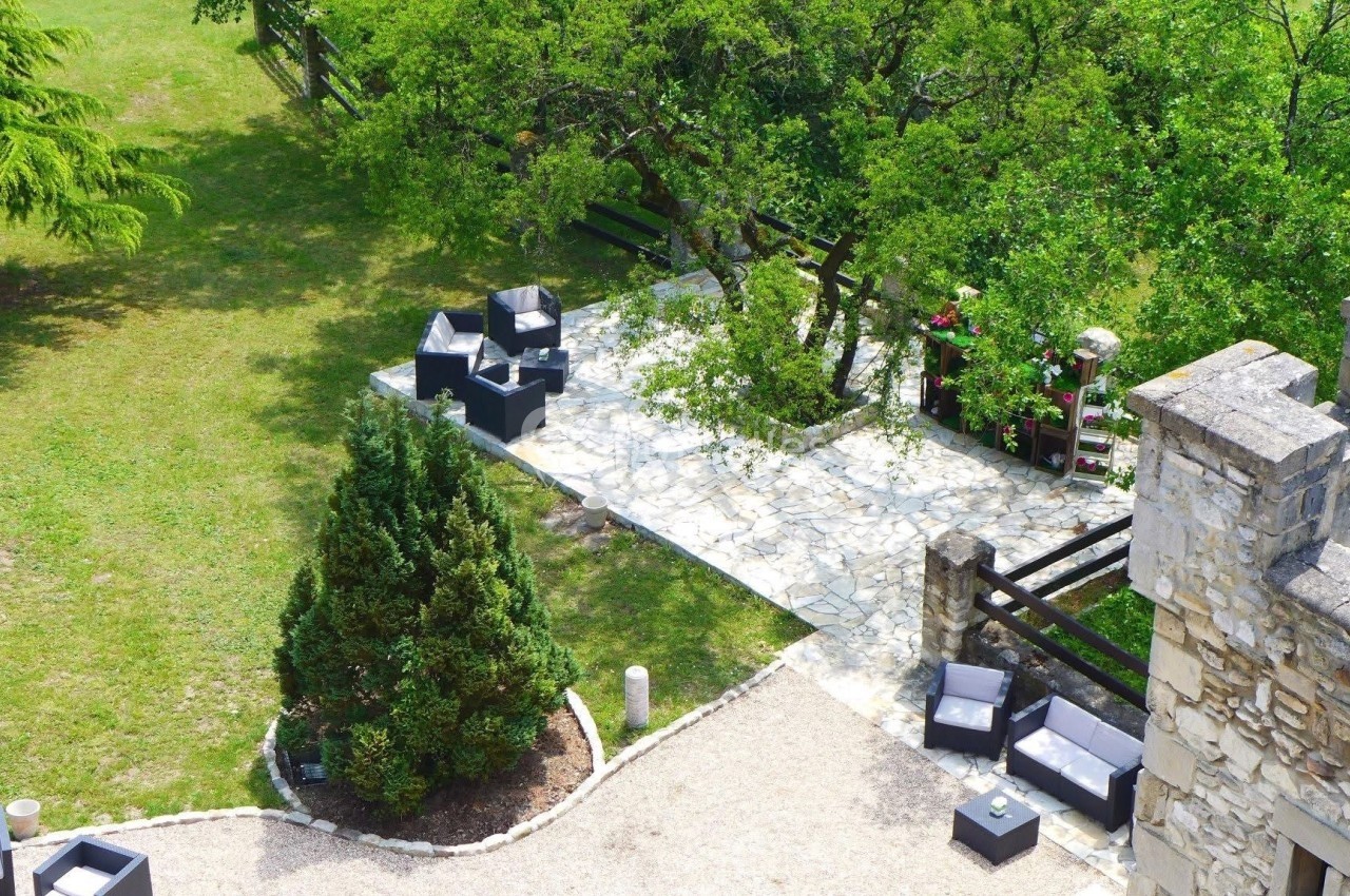 Terrasse en pierre avec mobilier de jardin, entourée de verdure et située près d'un bâtiment en pierre.