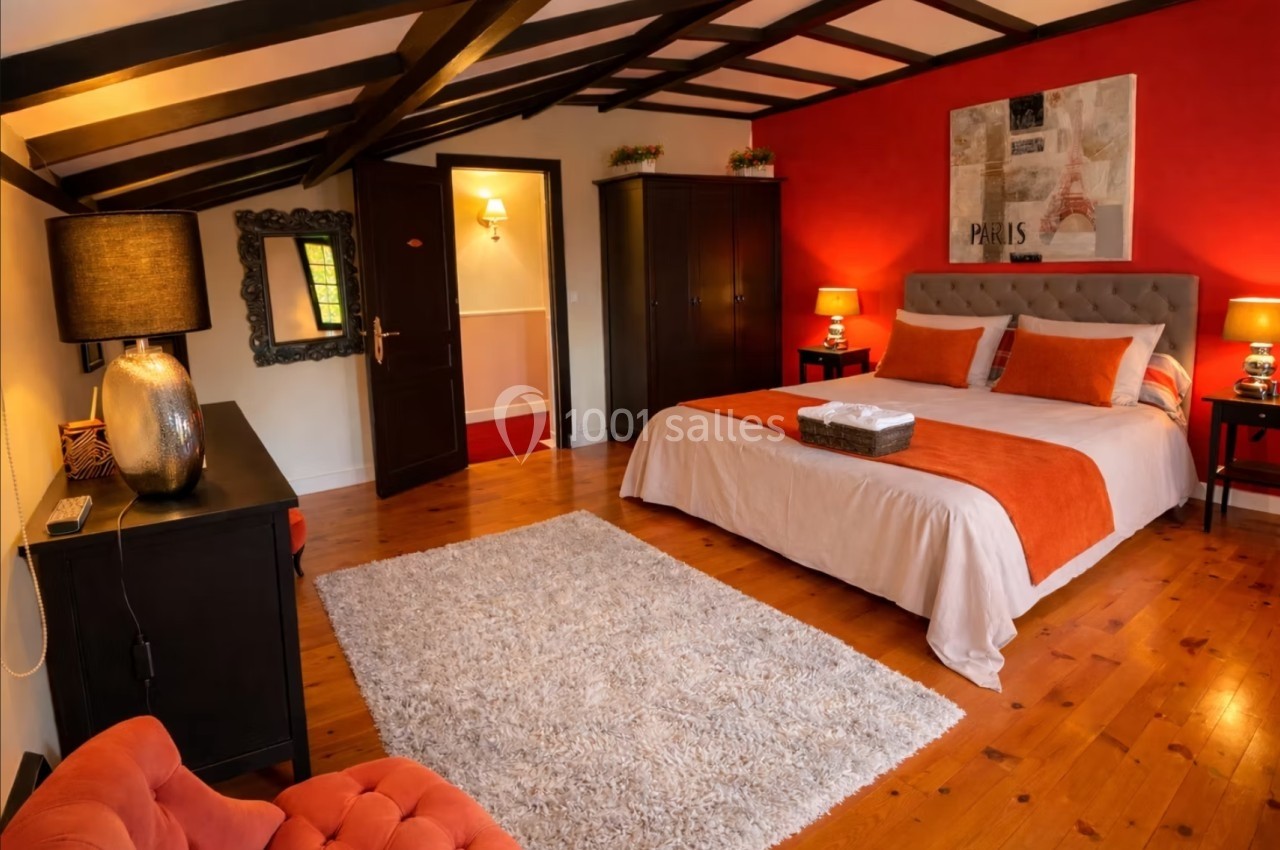 Chambre lumineuse avec lit double, murs rouges, meubles en bois sombre et tapis clair sur un sol en parquet.