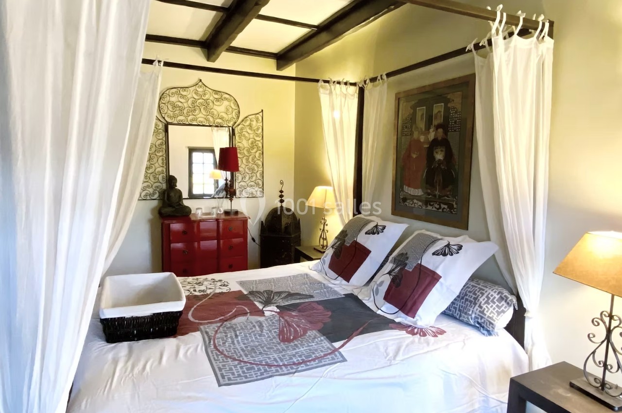 Chambre lumineuse avec lit à baldaquin, décorée de meubles rouges, lampes et tableaux muraux.