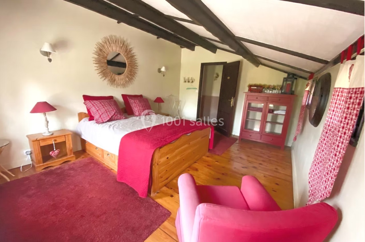 Chambre chaleureuse avec lit double, fauteuil rose, mobilier en bois et décoration rouge sur un sol en parquet.
