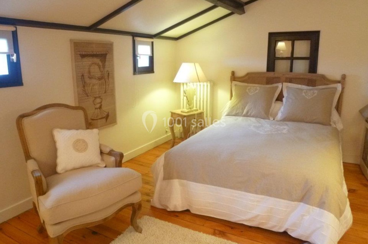Chambre mansardée avec lit double, fauteuil, lampe de chevet et parquet en bois clair.