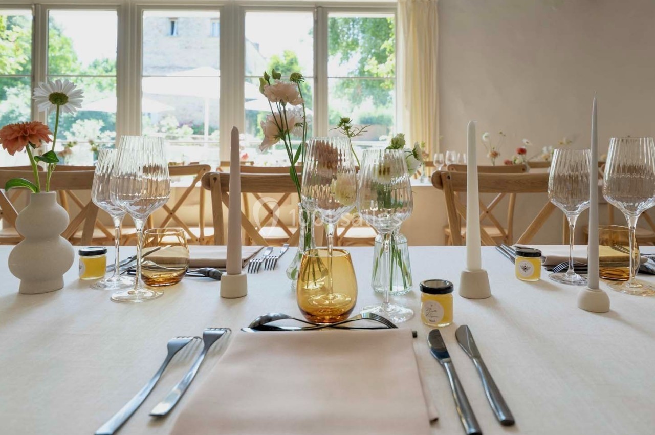 Table dressée avec élégance, comprenant verres, couverts, bougies et fleurs, devant une baie vitrée lumineuse.