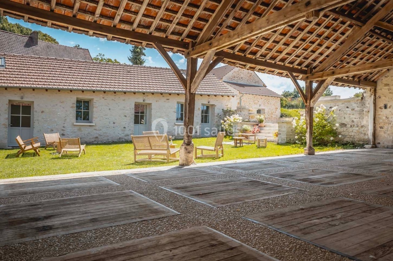 Cour intérieure avec pelouse, mobilier de jardin en bois et bâtiments en pierre sous un auvent en bois.